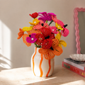 Fleurette, bouquet tropical en perles de rocaille orange, jaune et fuchsia à cœurs nacrés, dans un vase blanc rayé orange, fait main à Châteauroux, Perle Moi Ça