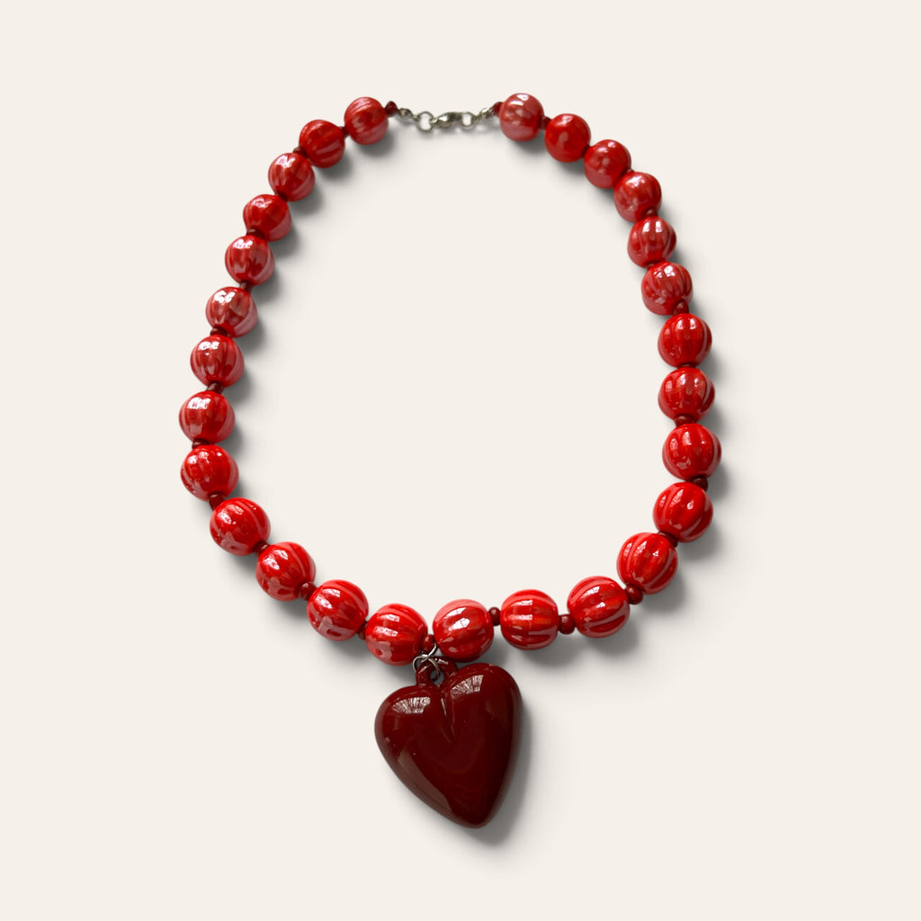 Collier de perles rondes rouges texturées et pendentif en forme de cœur bordeaux, présenté à plat sur fond neutre