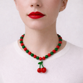 Josette, collier de perles rouges et vertes avec pendentif cerises, porté sur tee-shirt blanc, Perle Moi Ça