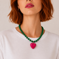 Josette, collier de perles vertes et rocailles roses avec grand cœur fuchsia, porté sur tee-shirt blanc, Perle Moi Ça