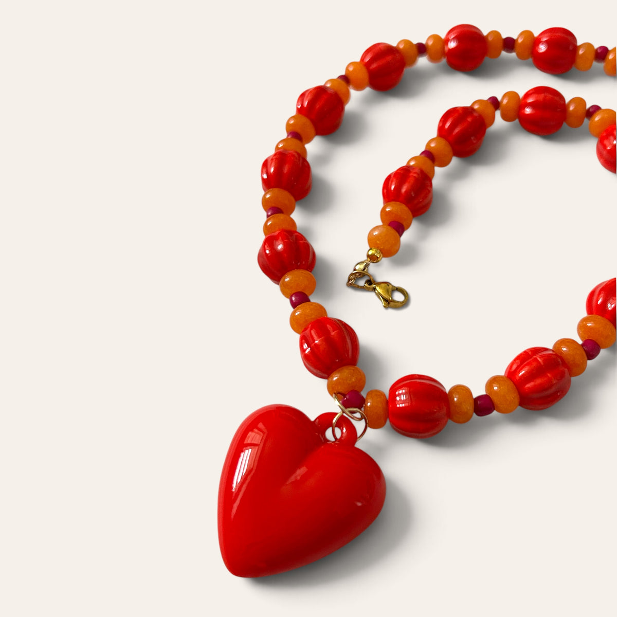 Détail du collier Josette Lux : grand cœur rouge, perles côtelées rouges et perles orange, fermoir doré, Perle Moi Ça