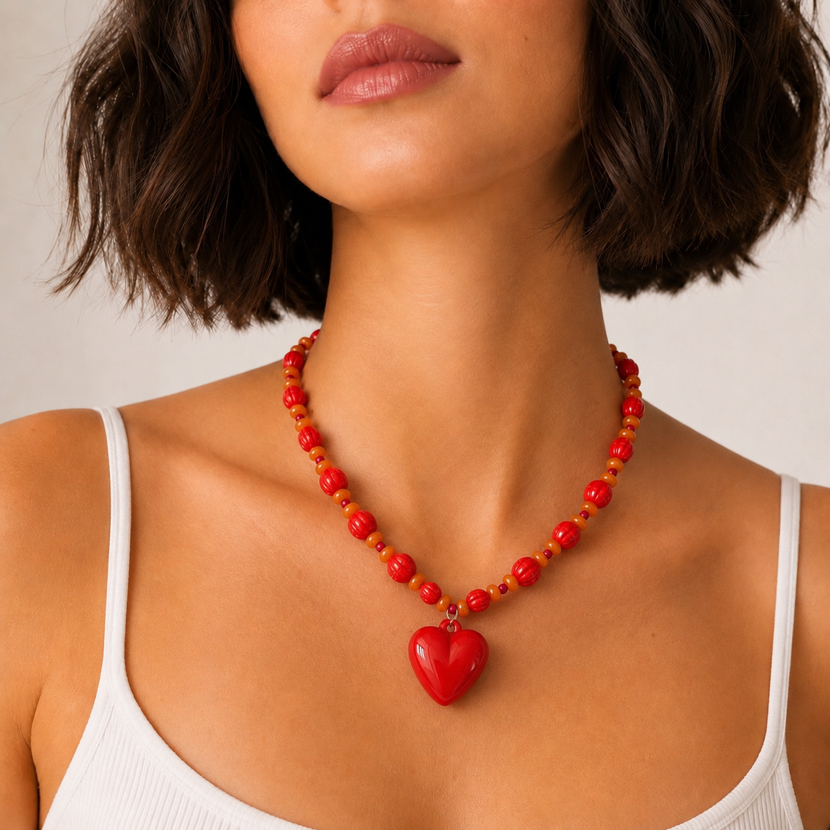 Josette Lux, collier de perles rouges et orange avec grand cœur rouge, porté sur débardeur blanc, Perle Moi Ça
