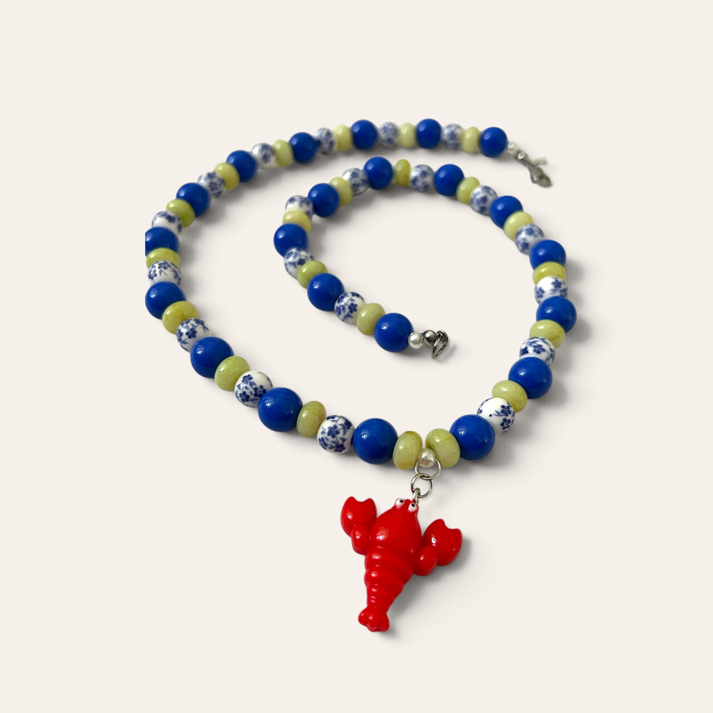 Détail du collier Josette Lux : petit homard rouge en acrylique, perles bleues et céramique fleurie, Perle Moi Ça