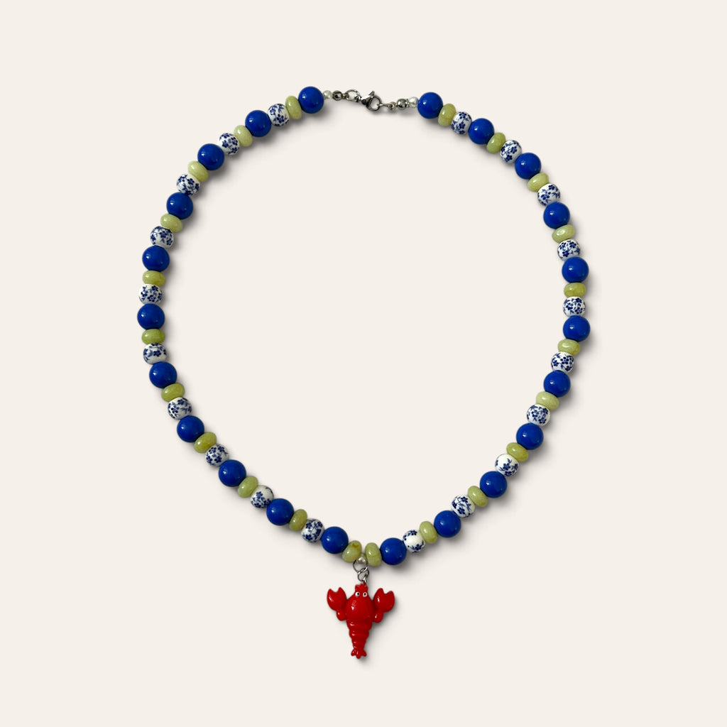 Josette Lux, collier tissé de perles bleues en acrylique, céramique fleurie et perles de verre vertes, à plat, Perle Moi Ça
