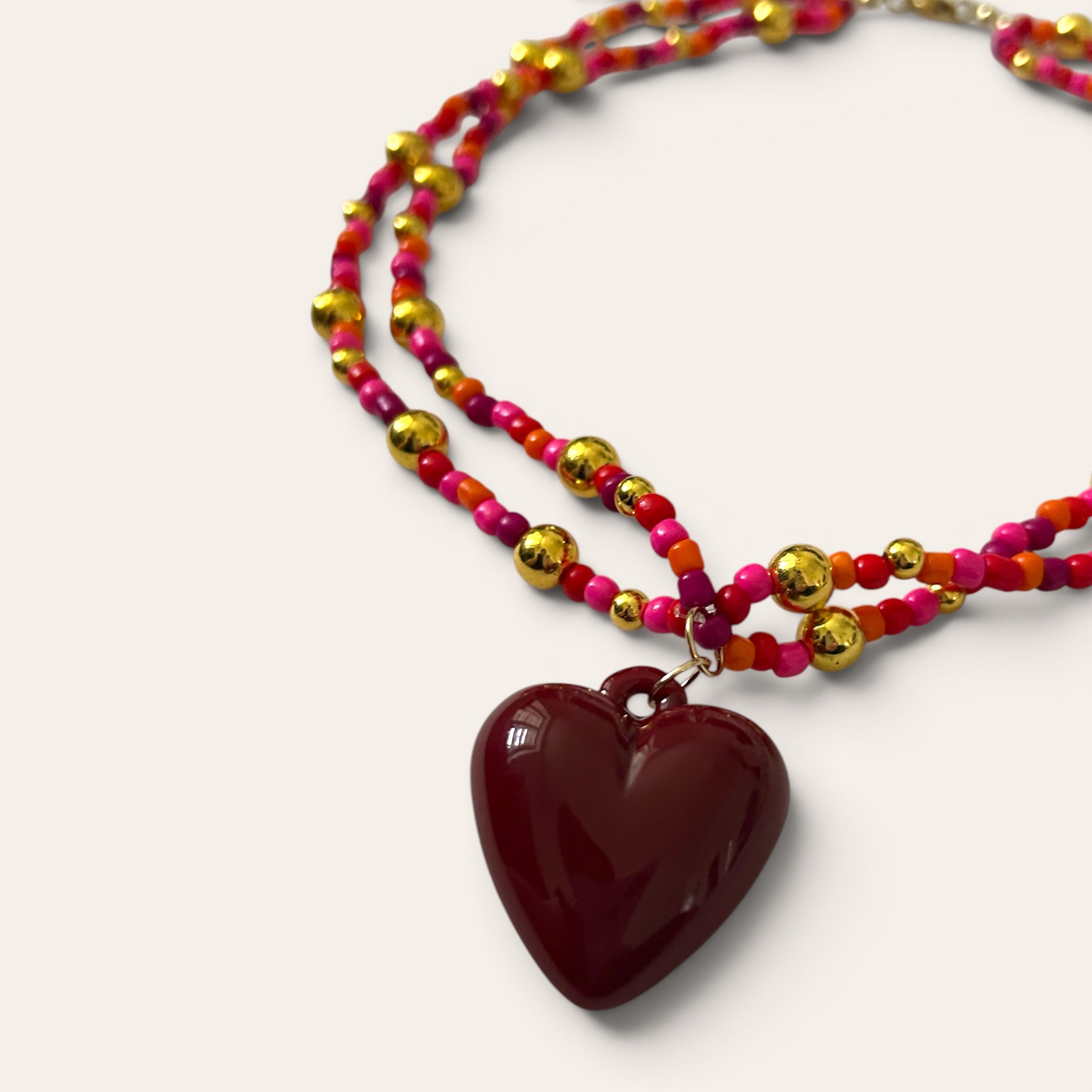 Gros plan pendentif cœur bordeaux acrylique, collier Linette fait main en perles de rocaille roses et oranges, Perle Moi Ça