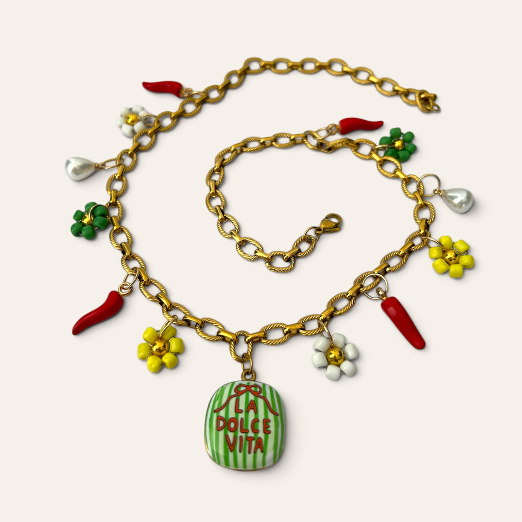 Pierette, collier à breloques en acier inoxydable doré posé à plat, médaillon La Dolce Vita, piments rouges, fleurs en perles de rocaille et gouttes nacrées, Perle Moi Ça