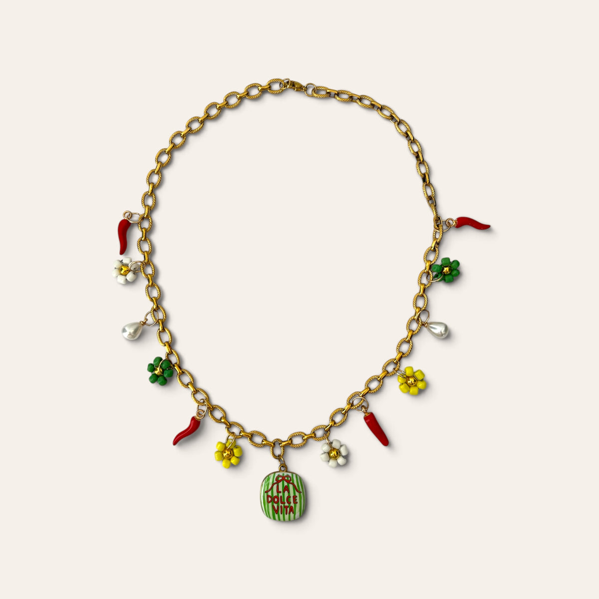 Pierette, collier à breloques présenté en cercle sur fond beige, chaîne dorée en acier inoxydable, breloques piments, fleurs tissées et gouttes nacrées, Perle Moi Ça