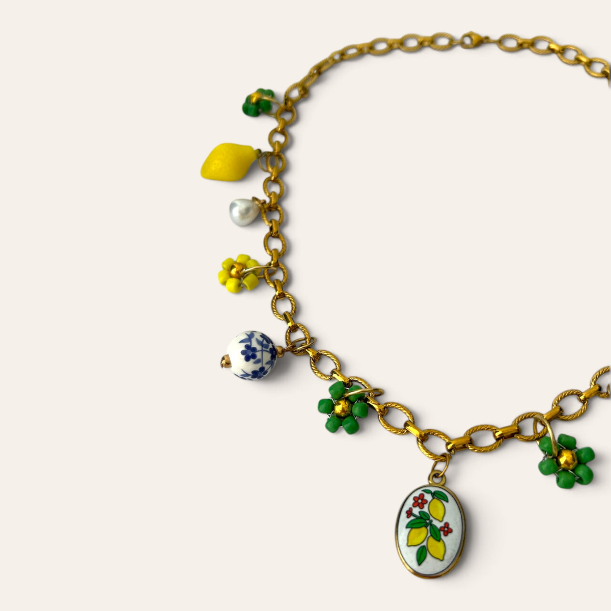 Détail du collier Pierette : médaillon citrons peint, citron jaune, perle de céramique bleue et fleurs tissées, Perle Moi Ça