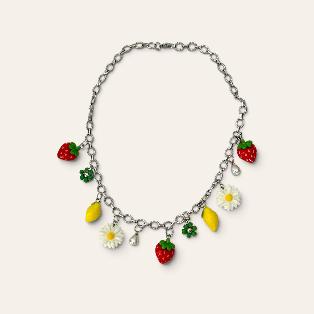 Pierette, collier chaîne argentée à breloques fraises, citrons, marguerites, fleurs vertes et perles, à plat, Perle Moi Ça